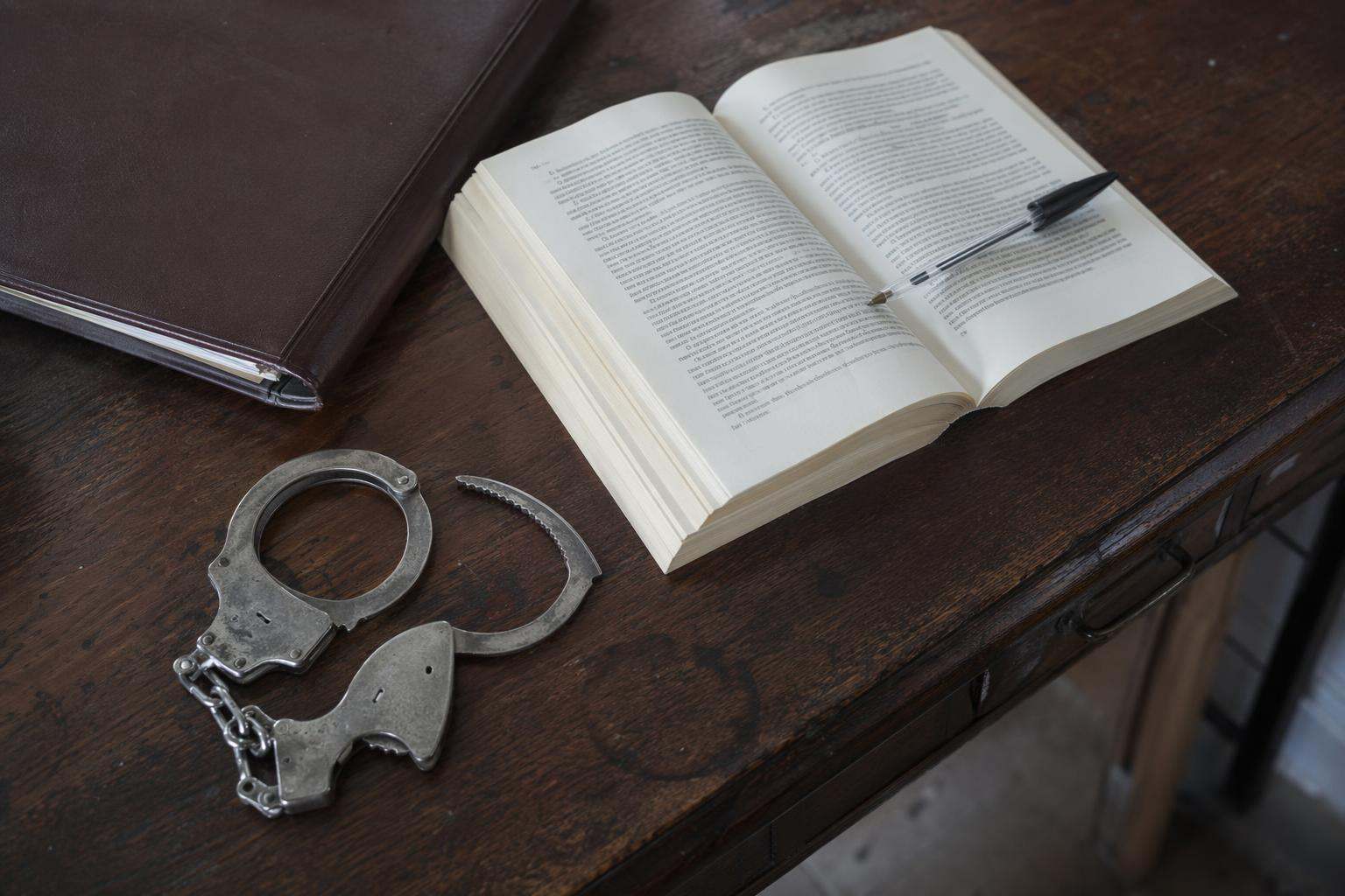 Esposas y código penal abierto sobre escritorio antiguo, abogados penalistas Ávila