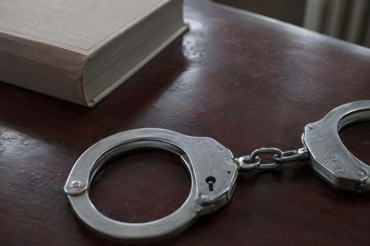 Esposas de acero sobre escritorio de mahogany oscuro en despacho de abogados penalistas en Tenerife