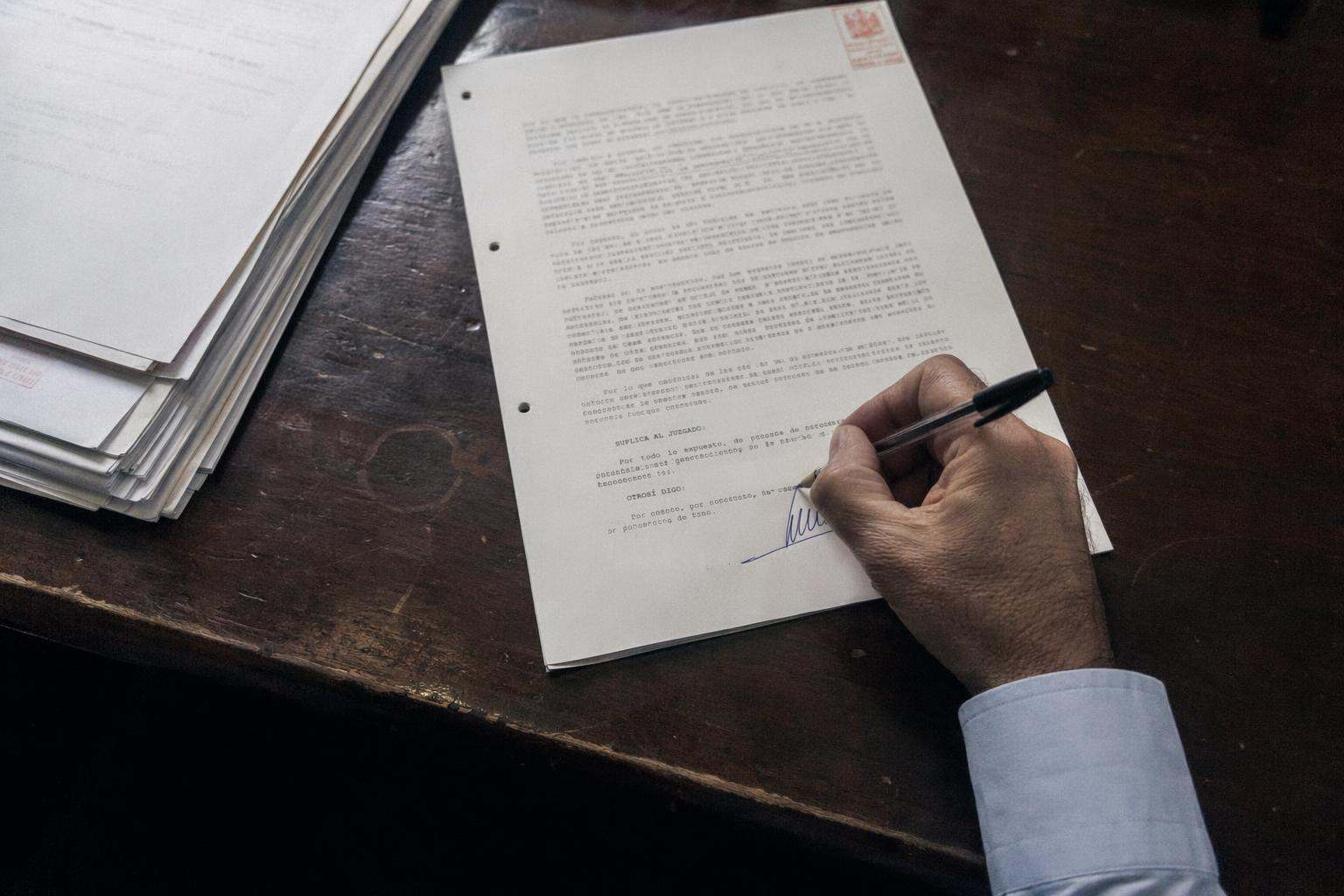 Detalle cenital de mano de abogado firmando escrito procesal con sello rojo, despacho sobrio, Recurso de Casación Penal