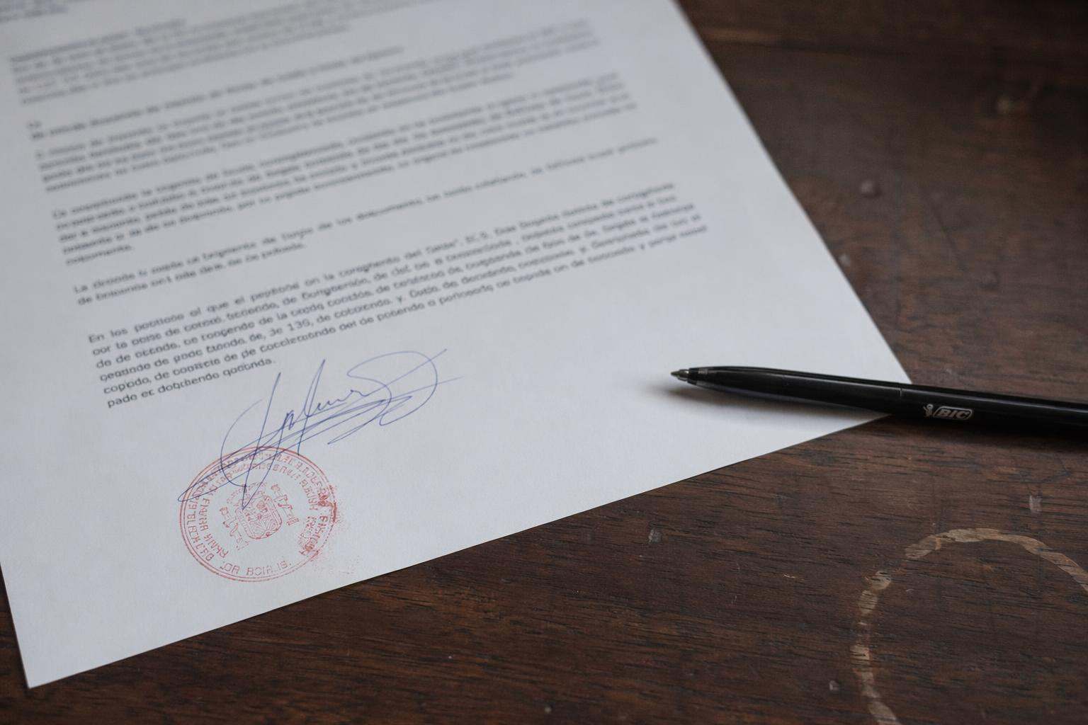 Sello procesal rojo sobre escrito firmado con bolígrafo en mesa de despacho de abogado penalista en Vitoria